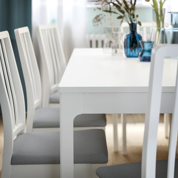Modern white extendable dining table set with grey cushioned chairs.