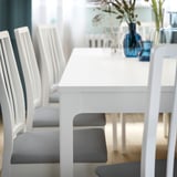 Modern white extendable dining table set with grey cushioned chairs.