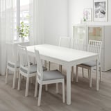 Minimalist white dining table with 6 gray-cushioned chairs, modern vertical-slat backs, set against a window.
