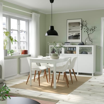 Modern dining area with green walls, white EKEDALEN table, chairs, and sideboard. Black lamp, large photo, clean style.