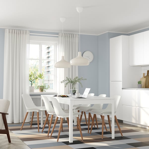 Modern dining room with white EKEDALEN extendable table and chairs, surrounded by white pendant lights and tall windows with white curtains.
