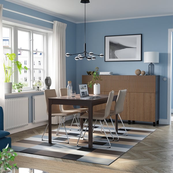 Modern dining room with blue walls, dark brown extendable table, metal chairs, large window, sideboard, and striped rug.