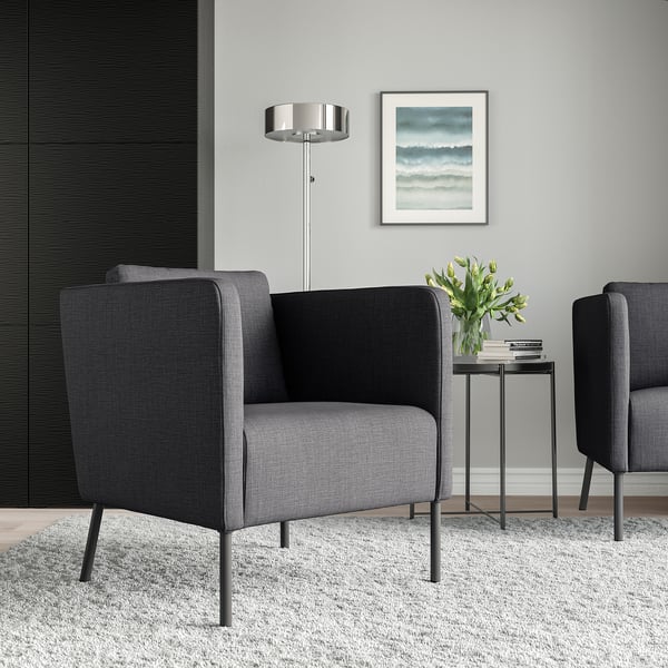 Gray EKERÖ armchair with dark legs, next to a side table with flowers and books. Light gray walls, floor lamp, small rug.