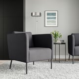 Gray EKERÖ armchair with dark legs, next to a side table with flowers and books. Light gray walls, floor lamp, small rug.