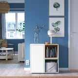 Modern blue room with white EKET storage unit. Vase with flowers, lamp, books, and framed plant art.