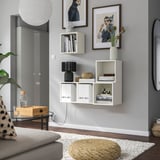 Modern living room with EKET shelves, books, flowers, and art. Grey wall, cozy couch, coffee table with water dispenser.