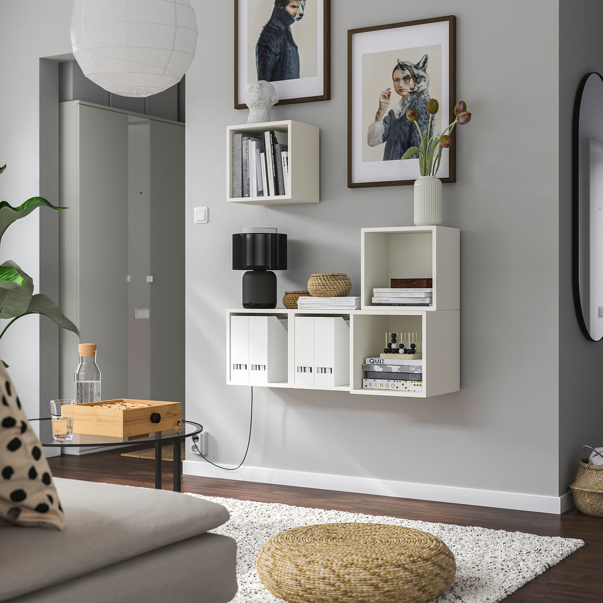 Modern living room with EKET shelves, books, flowers, and art. Grey wall, cozy couch, coffee table with water dispenser.