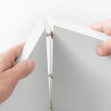 Hands assemble white EKET wall cabinet, showcasing easy setup and wall-mounting feature.