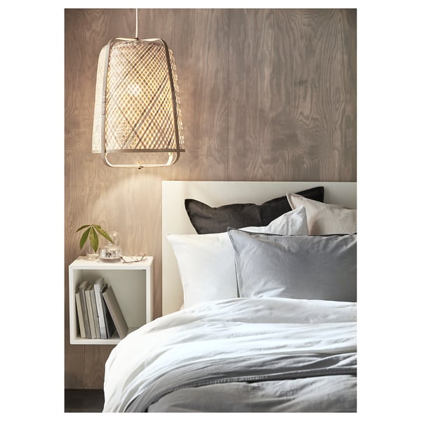 Modern bedroom with white bedding and pillows, hanging light fixture, and side unit shelf with books, jar, and plant.