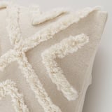 White cushion cover with textured, looped geometric design. Soft cotton with a hidden zipper for easy cleaning. Boho-style decor.