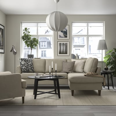 Modern living room with EKHOLMA beige sofa, coffee table, pillows. Large windows, plants, pendant light.