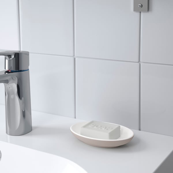 White oval soap dish on a bathroom counter, holding a bar of soap, next to a shiny chrome faucet. Part of the EKOLN series.