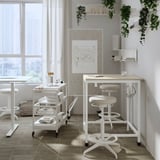 Modern white office setup with whiteboard, desk, and stools. Bright, minimalist design with plants.