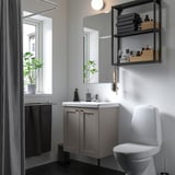 Modern bathroom with ENHET grey cabinets, white toilet, and open shelving. Mirror above sink, plants, and black floor.