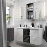 Modern bathroom with white ENHET vanity, mirror cabinets, and open shelves. Includes sinks, towels, and plants. Symmetrical design for shared space.