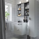 ENHET bathroom setup with white cabinet, mirror, black accents and grey tiles. Compact design, neat and modern.