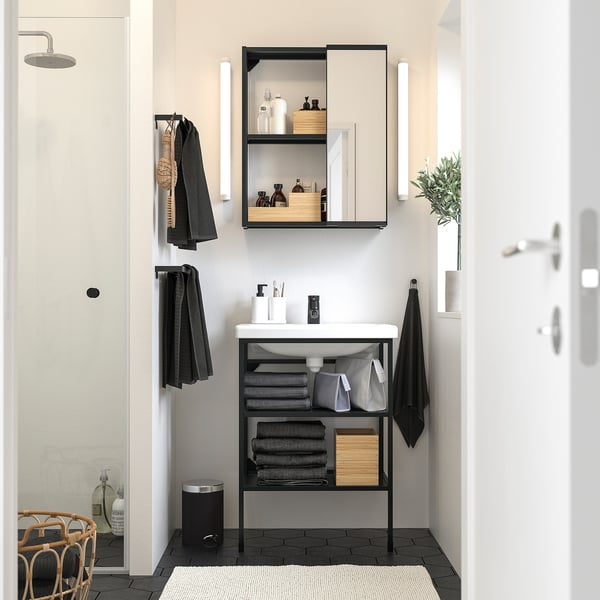 Modern minimalist bathroom with ENHET open shelf unit below sink, black accents, and mirrors above. Towels hang beside sleek shower.