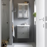Modern bathroom with grey ENHET vanity. Sink, mirror cabinet, plant, towels, shower. Compact yet functional.