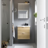Modern, light wood bathroom vanity with mirror cabinet. White counter, black accents. Sleek, compact design.