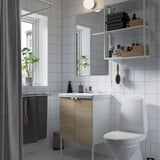 Small, modern bathroom with white tiles and a wooden vanity. A window, mirror, toilet, and open shelves.