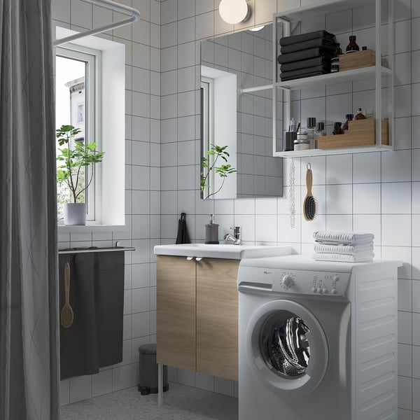 A modern bathroom with a white washing machine, wooden cabinets, and a mirror with open shelves.