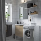 A modern bathroom with a white washing machine, wooden cabinets, and a mirror with open shelves.
