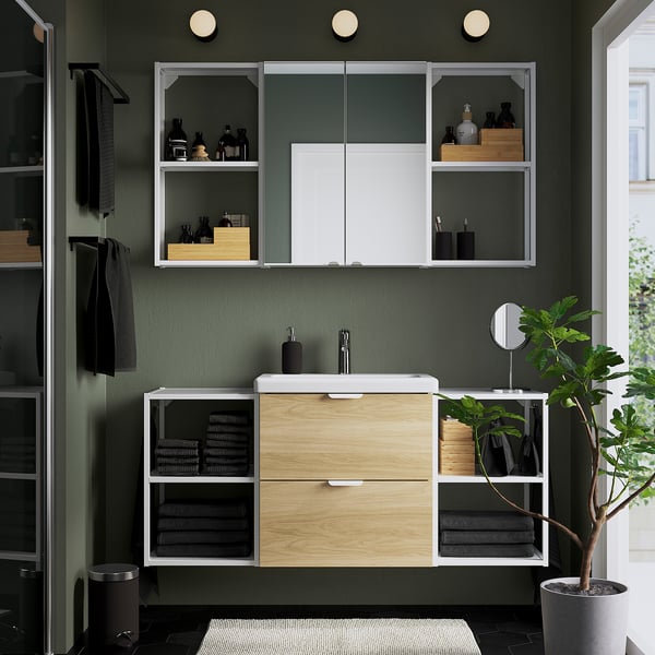 Modern bathroom vanity with light wood cabinet, white countertop, sink, and mirror. Plant and hanging towels highlight space and organization.