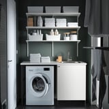 Green laundry room with ENHET, washing machine & sink. Organized with shelves and gray curtains. Length: 148 characters