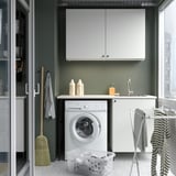 Small white laundry room with cabinets, washing machine, laundry basket, and drying rack.