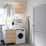 Modern laundry room with ENHET white washing machine, light wood cabinets, ironing board, and sink. Clean, organized, and minimalist design.
