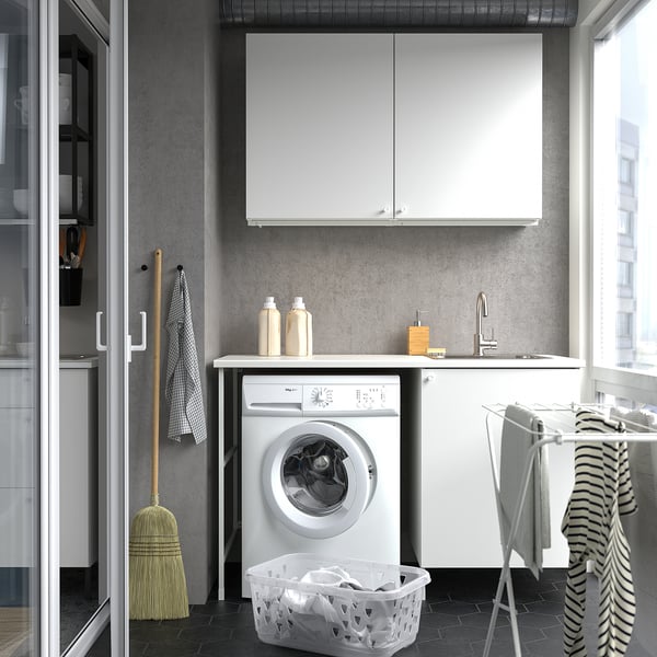 Modern laundry nook with ENHET cabinets, washing machine, sink, and drying rack by window.