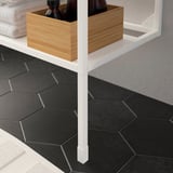 White ENHET shelf legs adjustable, holding wooden storage box with bottles, set on dark hexagonal floor tiles.