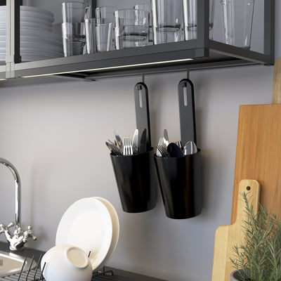 Wall-mounted storage rail holding cups and hanging containers with cutlery in kitchen.