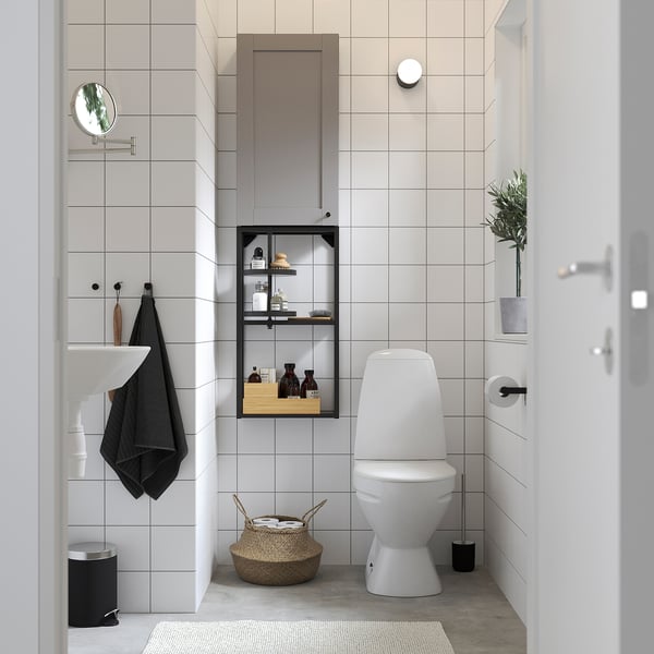 Modern bathroom with ENHET grey storage unit. Hanging mirror, round light, white toilet, wicker basket, black accents.