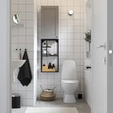 Modern bathroom with ENHET grey storage unit. Hanging mirror, round light, white toilet, wicker basket, black accents.