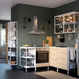 White ENHET kitchen unit with bowls, jars, pans. Wall-mounted oven, green walls, patterned floor.