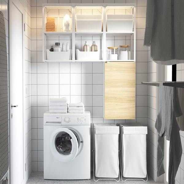 Modern, white laundry setup with ENHET shelving unit, washing machine, and drying baskets, efficiently utilizing space.