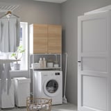 Wooden ENHET laundry setup with white washer, drying rack, and wicker basket. Compact and tidy for small spaces.