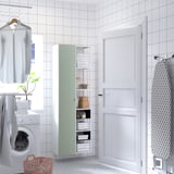 Minimalist laundry nook with ENHET green-and-white cabinet, washing machine, and ironing board.