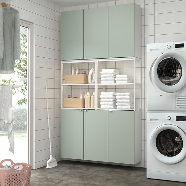 Modern laundry room with green cabinets, stacked washer/dryer, and tidy storage.