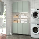 Modern laundry room with green cabinets, stacked washer/dryer, and tidy storage.