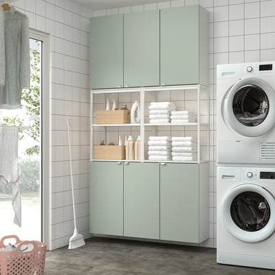 Modern laundry room with green cabinets, stacked washer/dryer, and tidy storage.