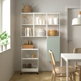 ENHET wall shelves, light grey-green, minimalist design, corner fit, holding items, near window, near chair.