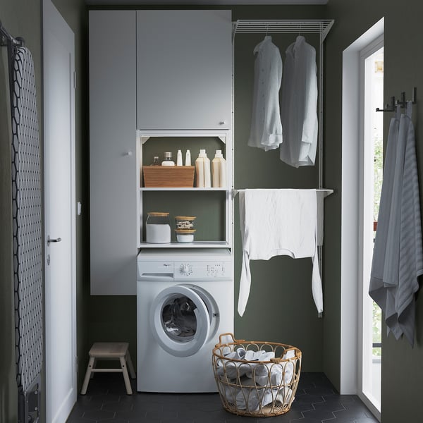 Small, modern laundry area with white ENHET units, washing machine, hanging garments, basket, and door.