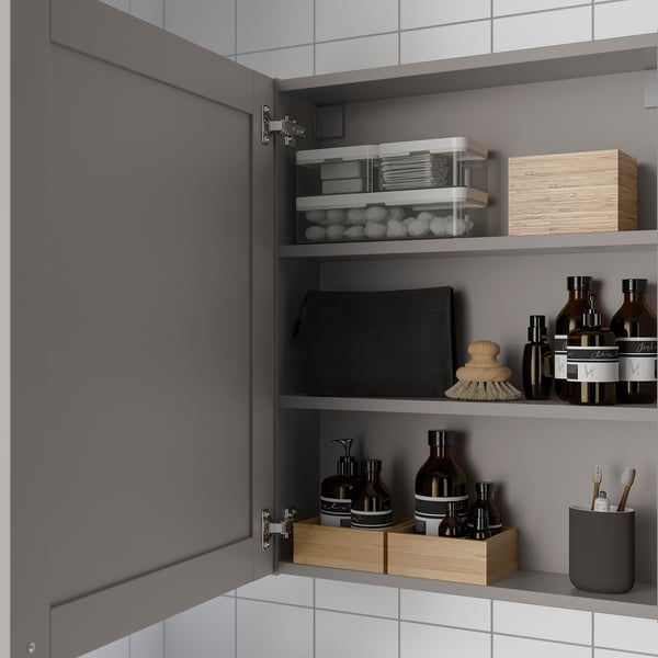 Open grey cabinet shows bathroom items: jars, bottles, and brushes on shelves, demonstrating organized storage.