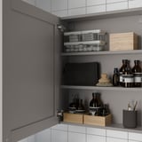 Open grey cabinet shows bathroom items: jars, bottles, and brushes on shelves, demonstrating organized storage.