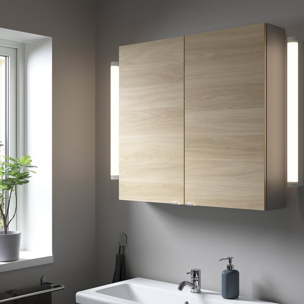 ENHET bathroom cabinet in light oak with mirrored doors and lighting. Includes sink and soap dispenser.