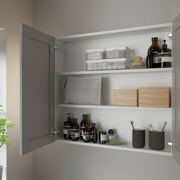 Open grey ENHET wall cabinet showing organized toiletries on three shelves, with one door fixed.