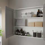 Open grey ENHET wall cabinet showing organized toiletries on three shelves, with one door fixed.