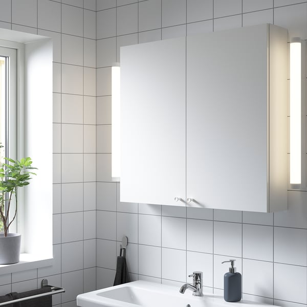 Modern bathroom featuring ENHET white wall cabinet with lights, containing a sink, soap dispenser, and plant.